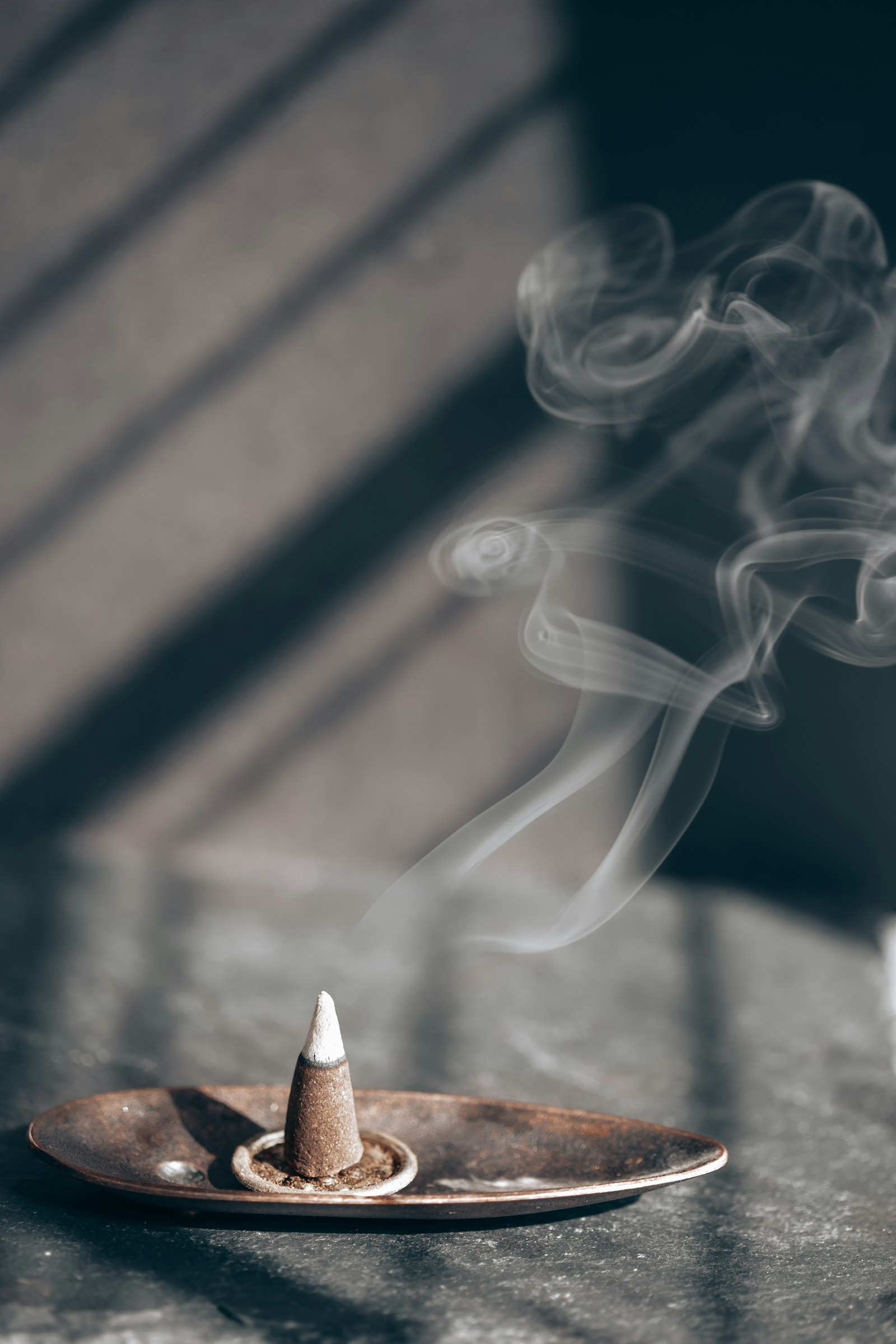 A lit incense stick with a thin wisp of smoke rising in warm light