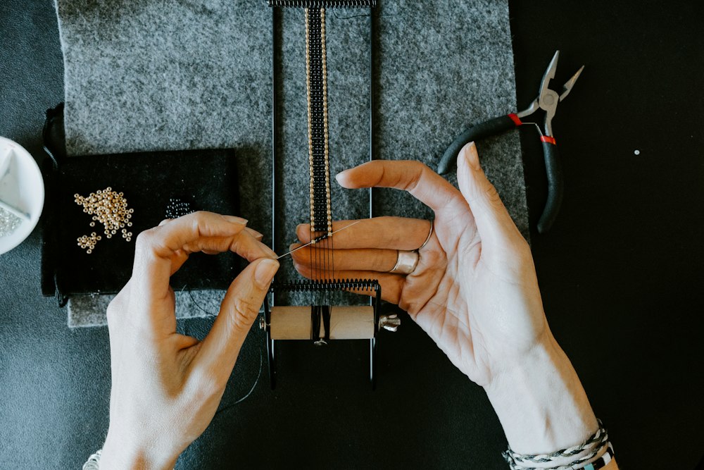 Hands knotting a cord bracelet at a workbench with craft tools