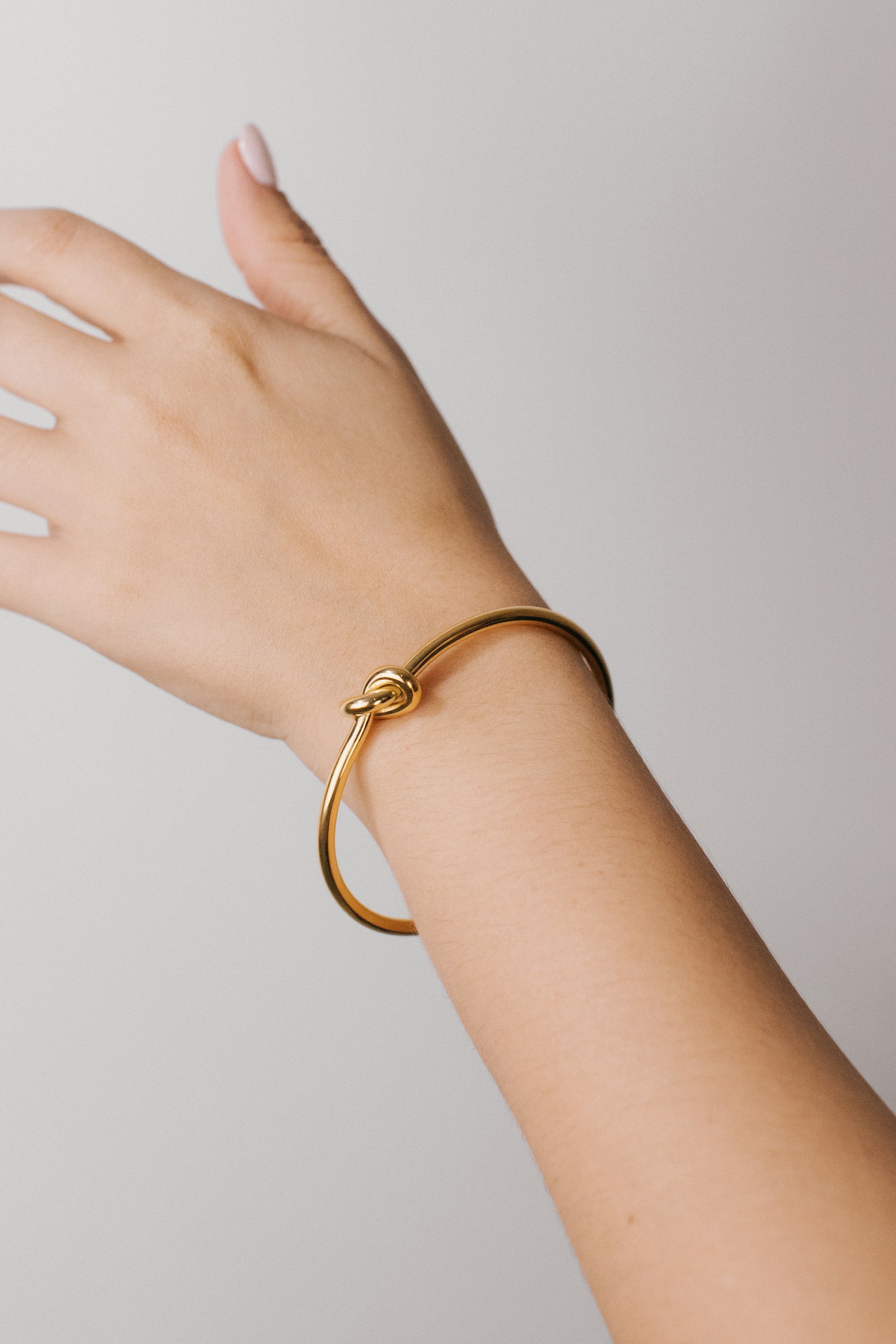 A wrist wearing a warm gold knot bracelet against soft ivory fabric