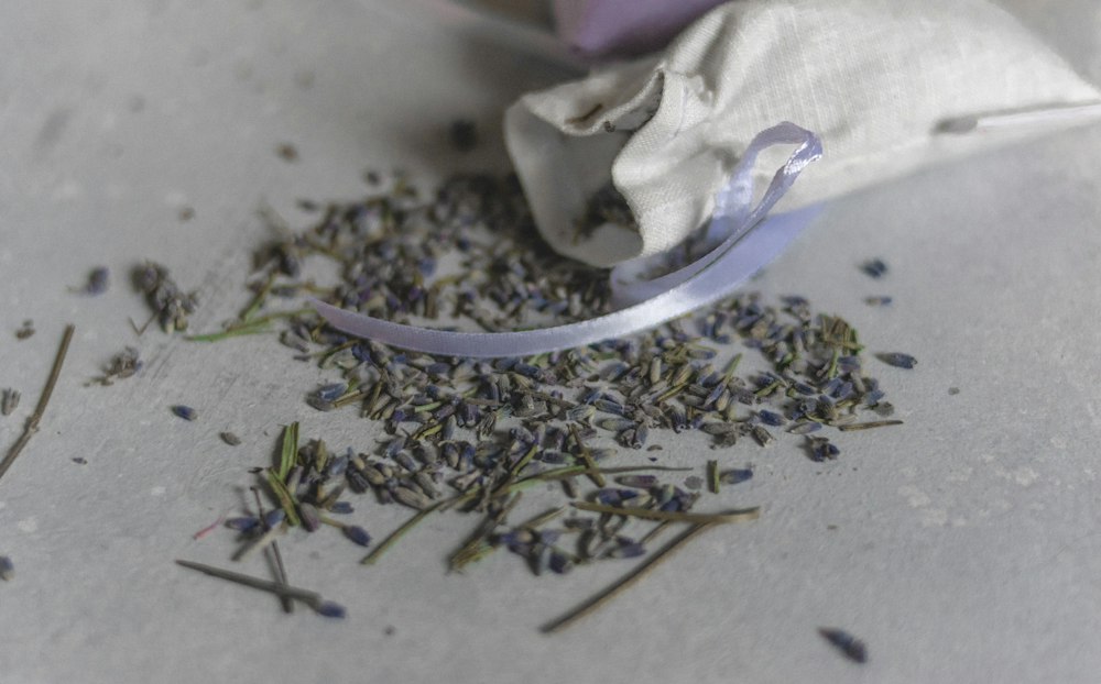 A small fabric bag filled with lavender seeds beside a wooden scoop